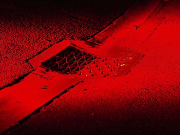 A stormwater drain in a bitumen footpath, illuminated by red light.